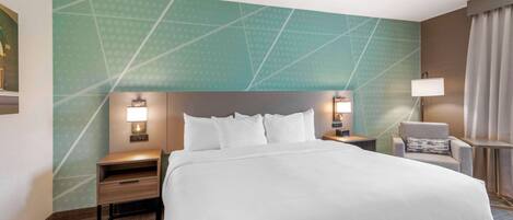 Habitación de hotel con una cama grande, dos mesitas de noche, una silla y una pared con diseños geométricos.