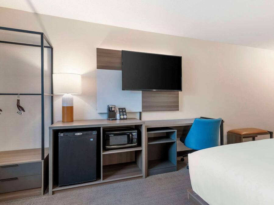 Quarto de hotel com cama, escrivaninha com computador, micro-ondas e mini geladeira.