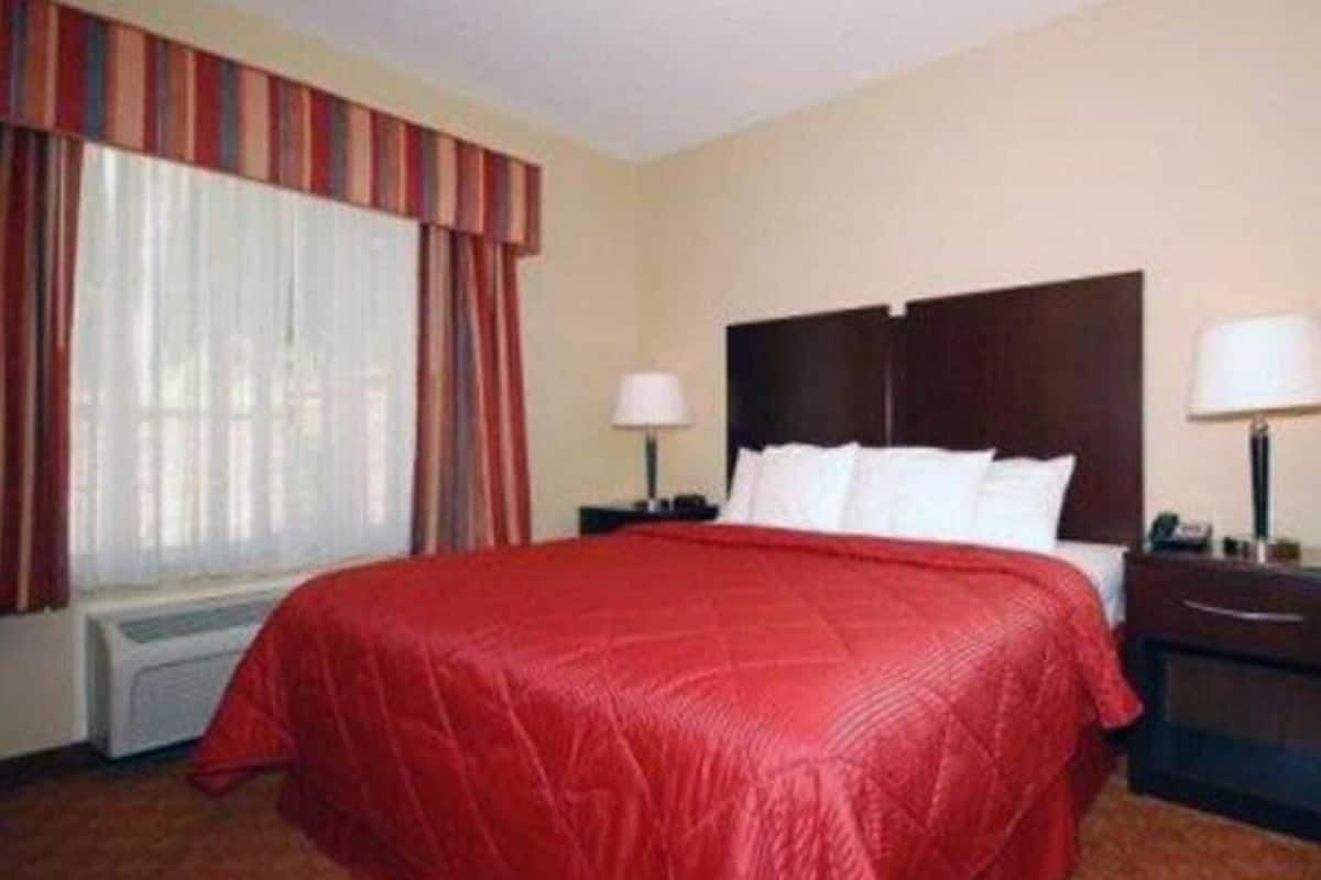 Ein Hotelzimmer mit einem großen Bett, zwei Nachttischen, einem Fenster mit Vorhängen und einer Heizung.