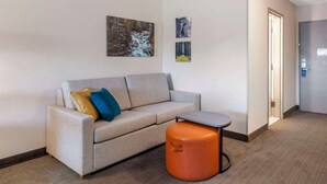 Una camera d'albergo moderna con un divano color beige, un poggiapiedi arancione e un tavolino in legno.