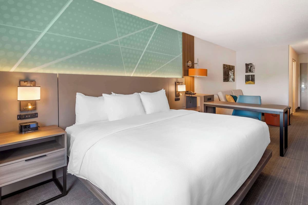 Ein Hotelzimmer mit einem großen Bett, Nachttischen mit Lampen, einem Schreibtisch und einem Sessel.