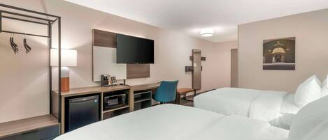 A hotel room with two beds, a desk, a chair, a television, and a small kitchenette.