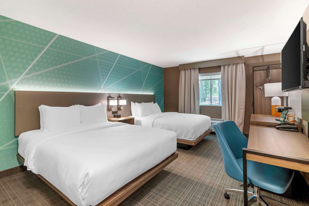 Ein Hotelzimmer mit zwei Betten, einem Schreibtisch, einem Sessel, einem Fernseher und einem Fenster mit Vorhängen.