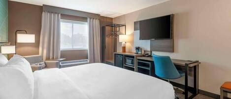 Una habitación de hotel con una cama grande, un escritorio con silla, televisión y una ventana con cortinas.