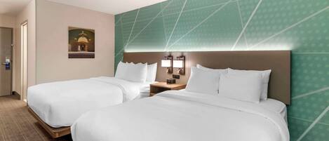 A hotel room with two beds, a nightstand with a lamp, and a wall-mounted artwork.