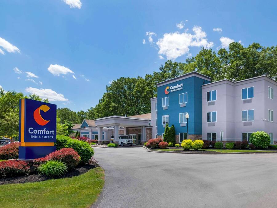 Un hotel Comfort Inn & Suites con facciata blu e bianca, area di parcheggio coperta e verde curato.
