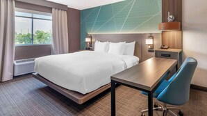 Una camera d'albergo con un letto, una scrivania, una sedia, una finestra con tende e un muro con motivo geometrico.