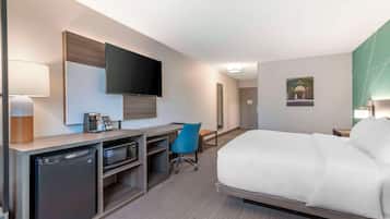 A hotel room with a bed, desk, chair, television, and a small refrigerator.