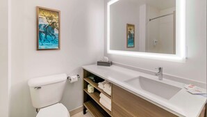 Un bagno moderno con il water bianco, un lavandino con uno specchio e un quadro appeso al muro.