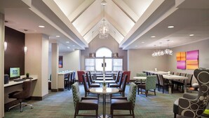 A hotel dining area with multiple tables and chairs, a central chandelier, and a view of the dining area through a large window. - Residence Inn by Marriott Toronto Markham (Markham)