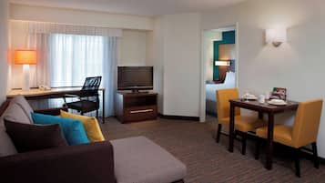 Une chambre d’hôtel comprenant un canapé, une télévision, un bureau avec une lampe et un coin repas avec des chaises et une table.