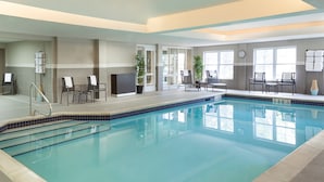An indoor swimming pool with clear water, surrounded by lounge chairs and tables, and a clock on the wall. - Residence Inn by Marriott Toronto Markham (Markham)