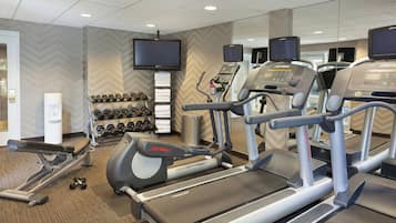 Un gimnasio con cintas de correr, mancuernas y un televisor.