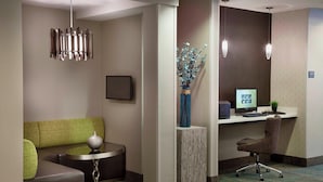 A modern hotel room with a green sofa, a small round table, a decorative vase, a desk with a computer, and a chair. - Residence Inn by Marriott Toronto Markham (Markham)