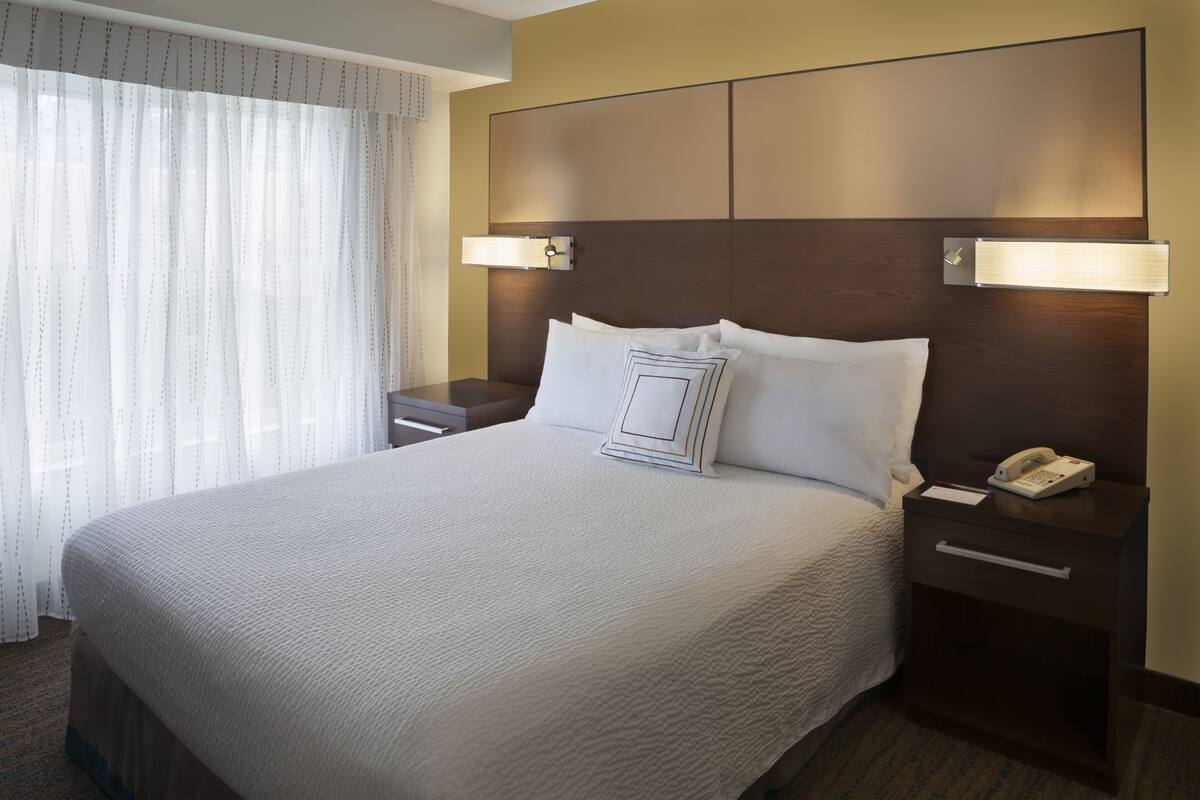 A hotel room with a large bed, two bedside tables, a nightstand, and a window with curtains.