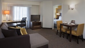 A hotel room with a sofa, a TV, a desk with a chair, and a dining table with chairs. - Cambridge Suites Mississauga (Mississauga)