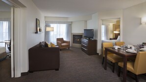 A hotel room with a living area, a dining table set for two, a sofa, a television, and a fireplace. - Cambridge Suites Mississauga (Mississauga)
