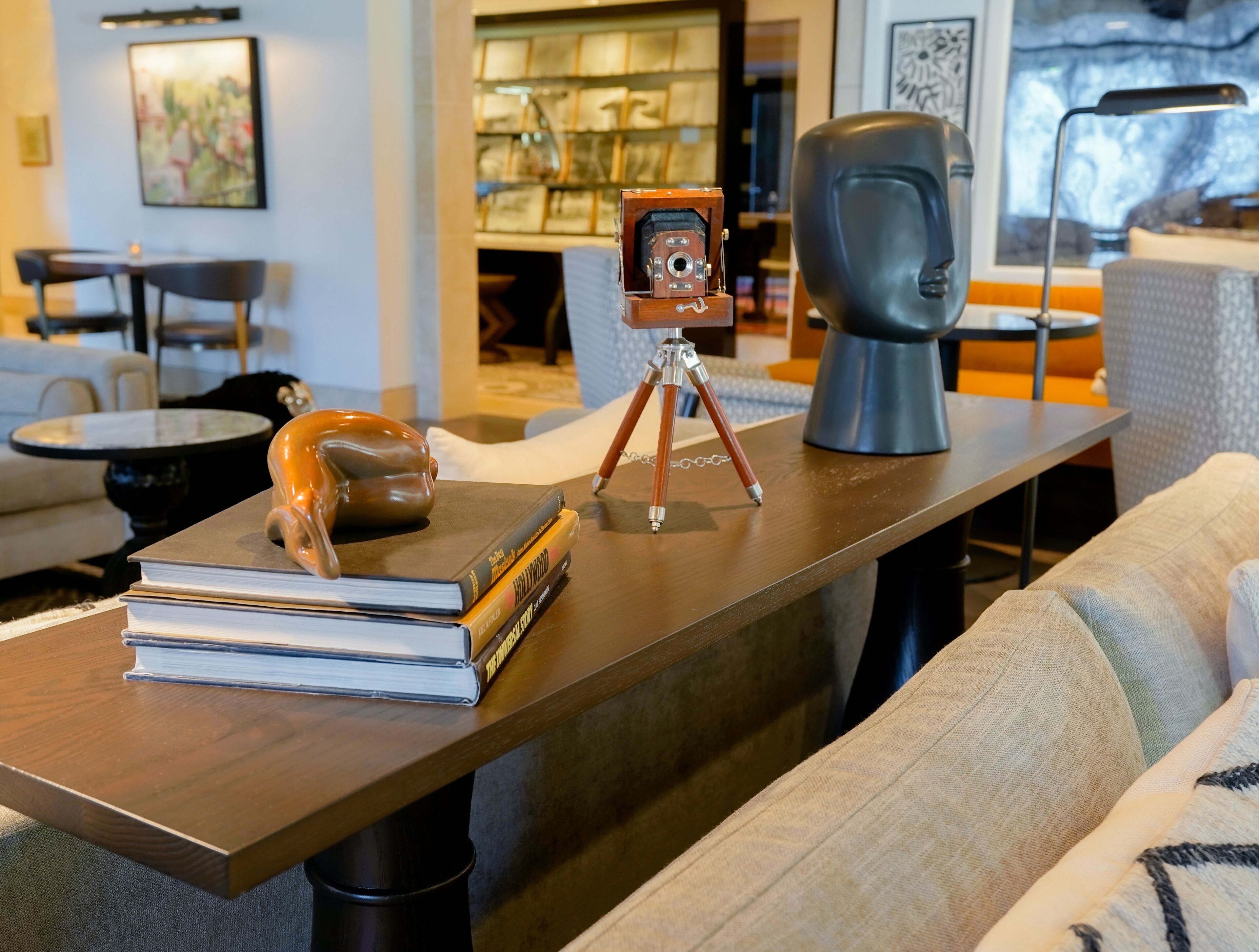 A wooden table with a camera on a tripod, a bust sculpture, and books.