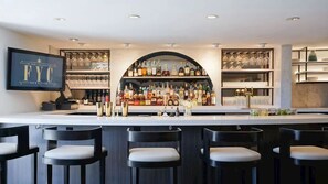 Een bar met een toog, krukken en flessen op de planken.