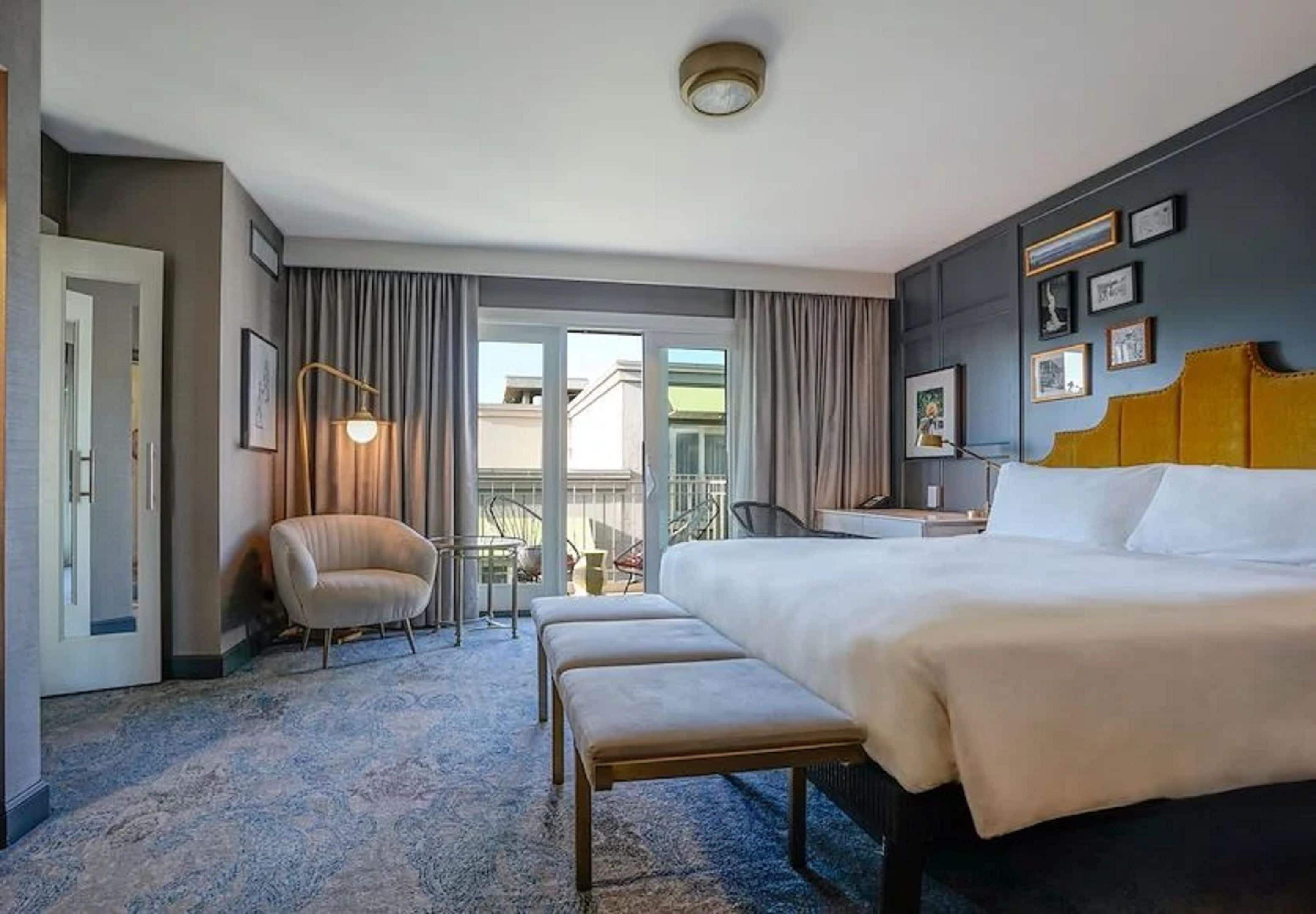 Ein Hotelzimmer mit einem großen Bett, einem Sessel, einem Schreibtisch und Blick ins Freie.