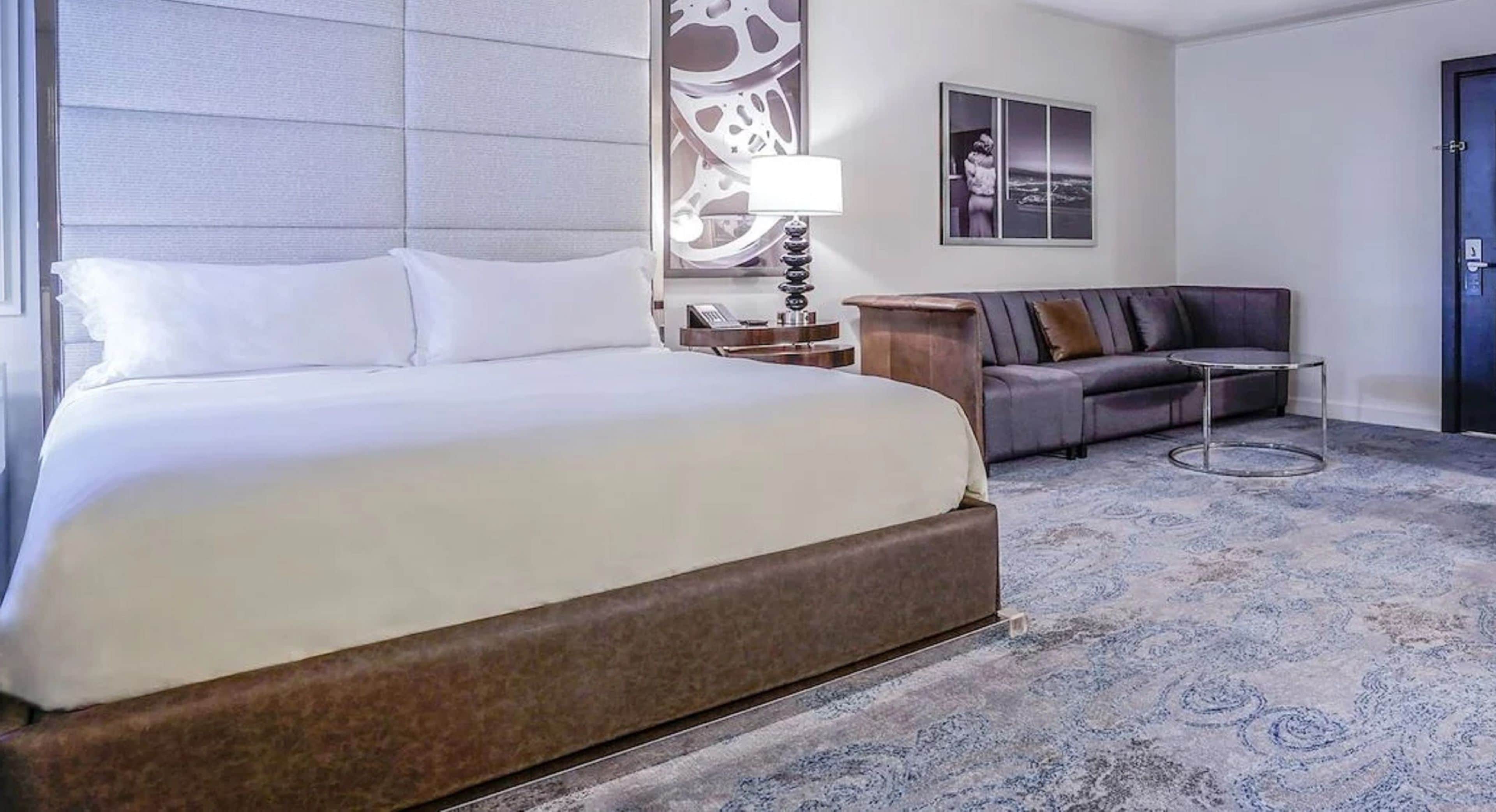 Habitación de hotel con una cama grande, un sofá, una mesita y una alfombra estampada.