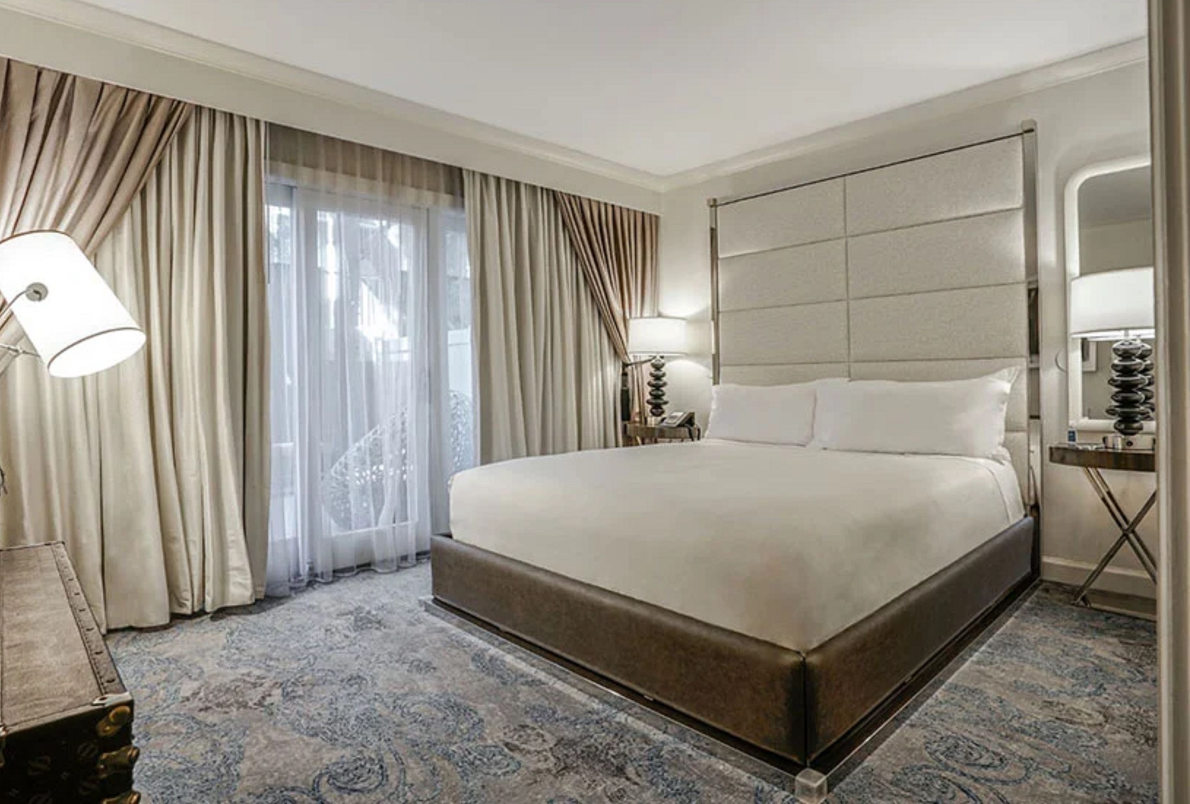 Una habitación de hotel con una cama grande, una mesita de noche con lámpara y un espejo.