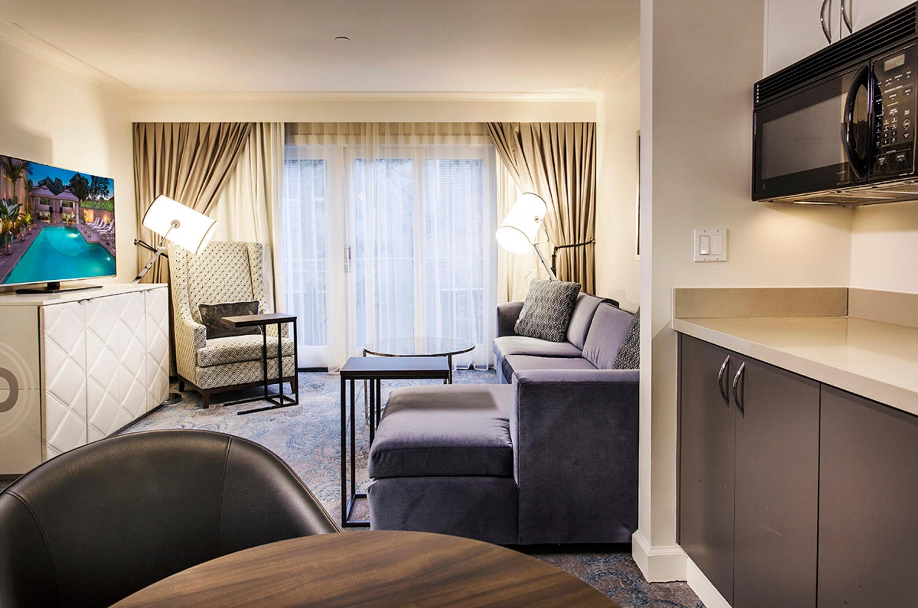 Habitación de hotel con sofá, sillón, mesa de comedor y televisión de pantalla plana.