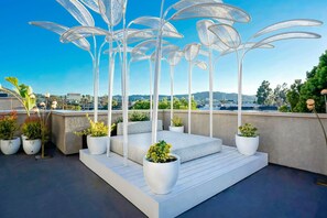 Een terras op het dak met witte metalen stoelen, potplanten en een helder uitzicht over de stad.