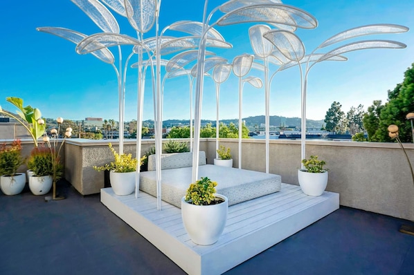Una terraza en la azotea con sillas de metal blanco, plantas en macetas y una vista despejada del horizonte urbano.