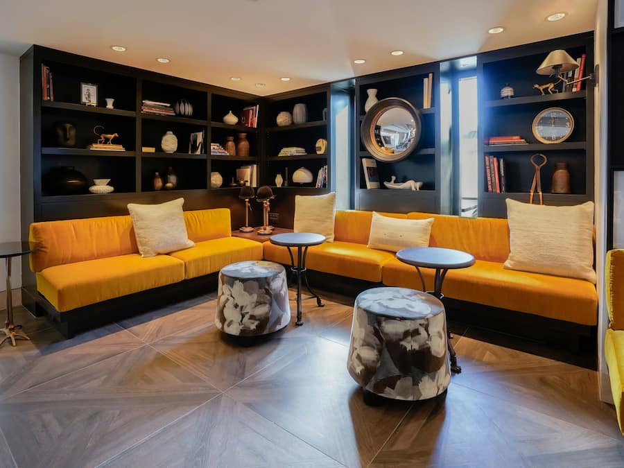 A modern lounge area with a yellow sofa set, round coffee tables, and a dark bookshelf filled with books and decorative items.