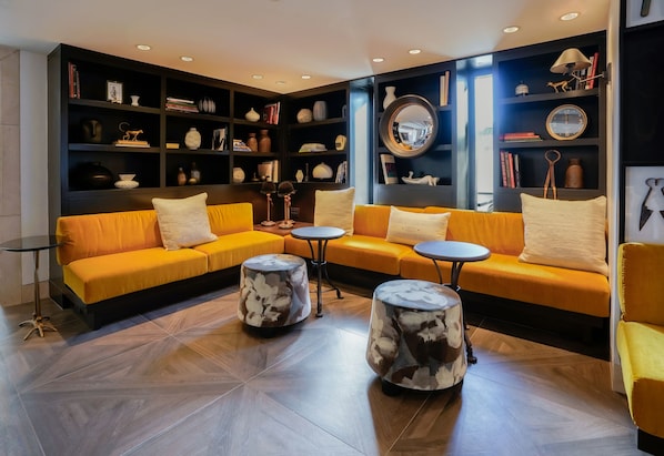 Ein stilvoller Lounge-Bereich mit einem gelben Sofagarnitur, runden Couchtischen und einem dunklen Bücherregal, gefüllt mit Büchern und Dekorationsobjekten.