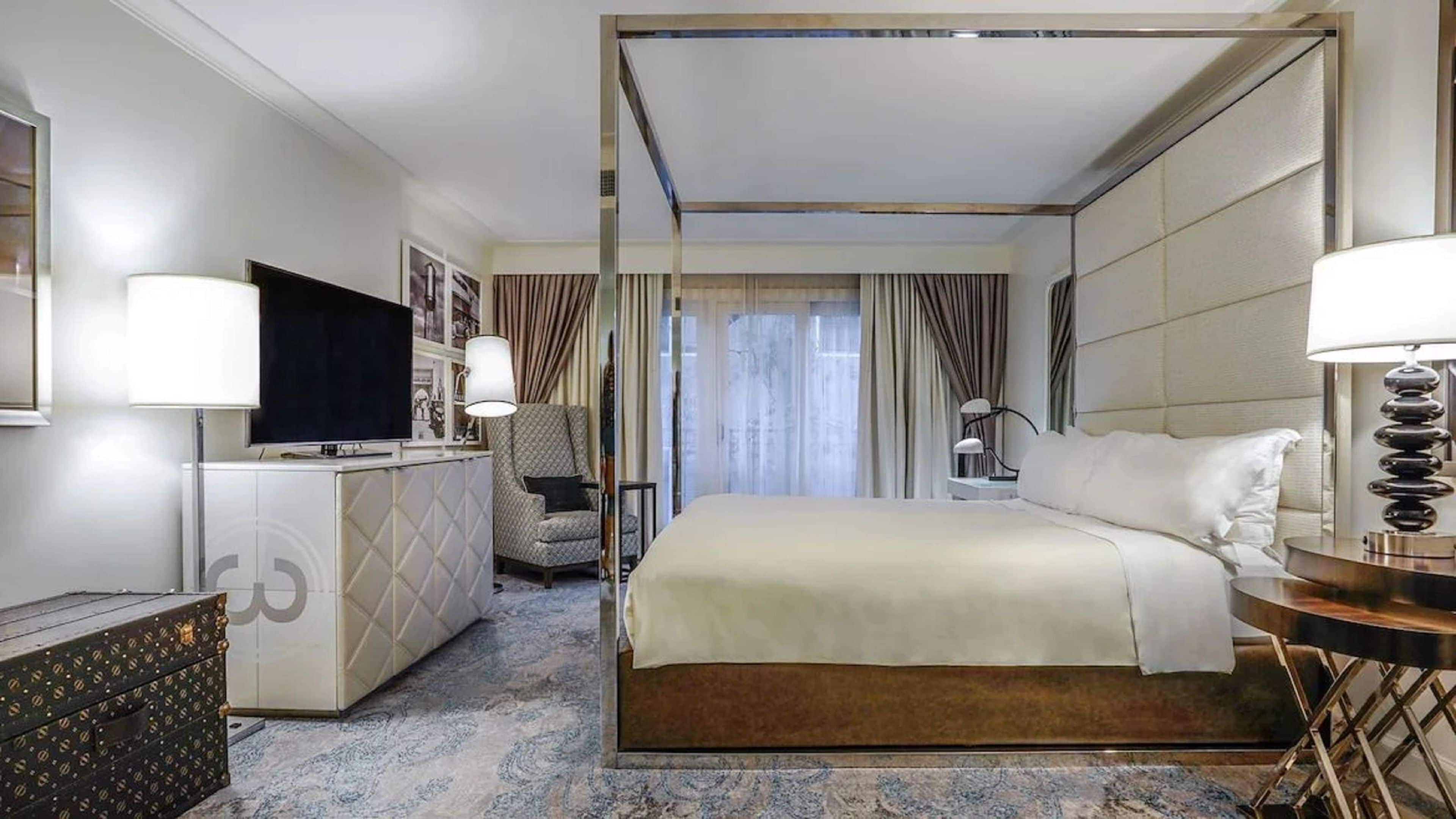 Una habitació d'hotel amb un llit, un escriptori, una televisió, una cadira i una làmpada.