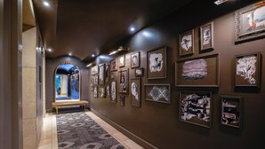 A hallway with a patterned carpet, framed artwork on the walls, and a bench. - Hotel Amarano Burbank - Hollywood (Burbank)