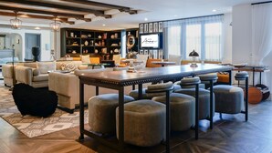 A modern bar area with a long table and multiple stools, a bookshelf filled with decorative items, and a large mirror on the wall. - Hotel Amarano Burbank - Hollywood (Burbank)