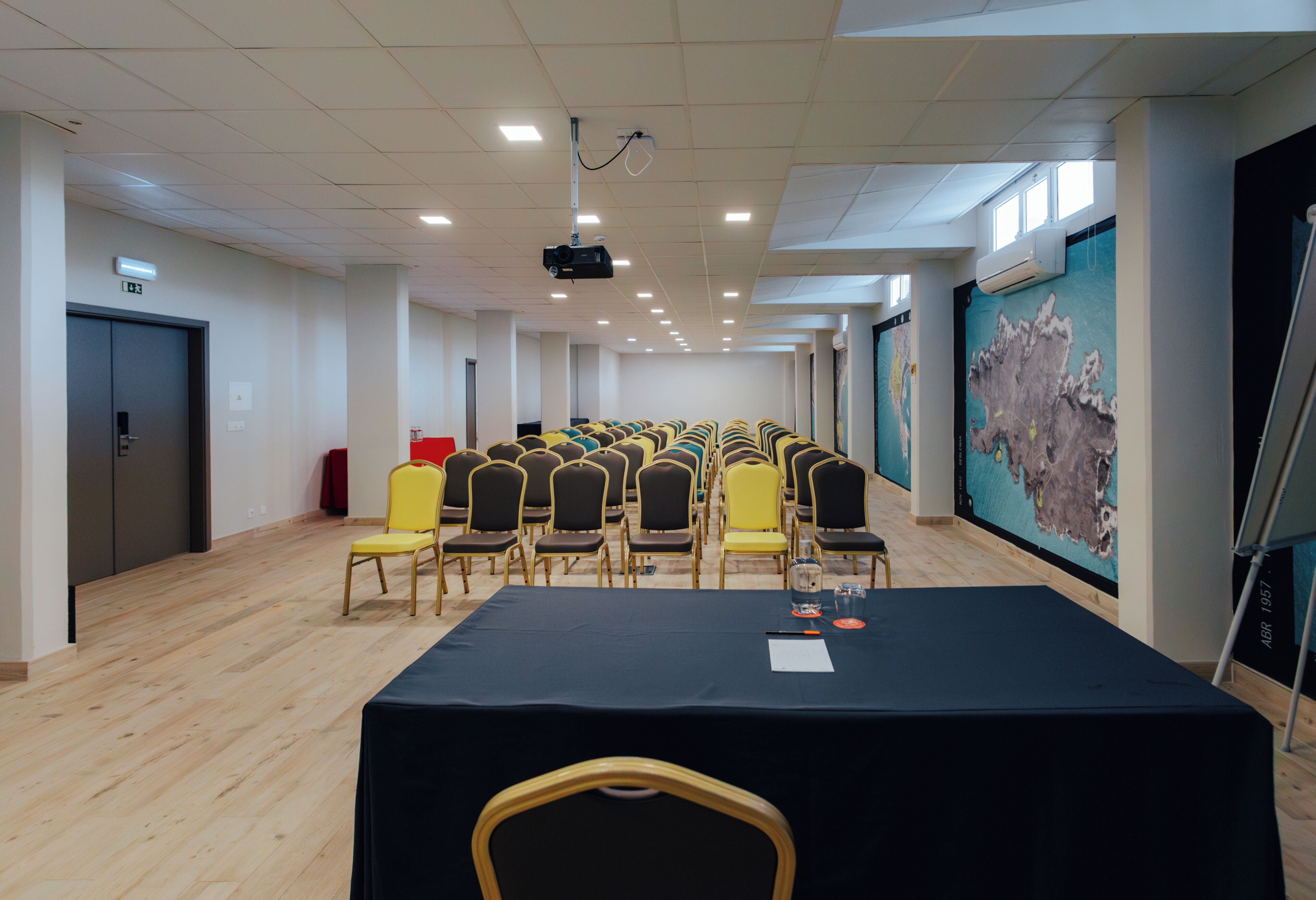 Un salón de conferencias con filas de sillas, un proyector y un mural grande en la pared.