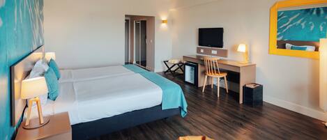 A hotel room with a bed, desk, chair, television, and a small seating area.