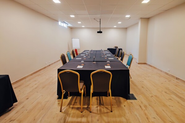 Un salón de conferencias con una larga mesa, sillas y una pantalla para proyector.