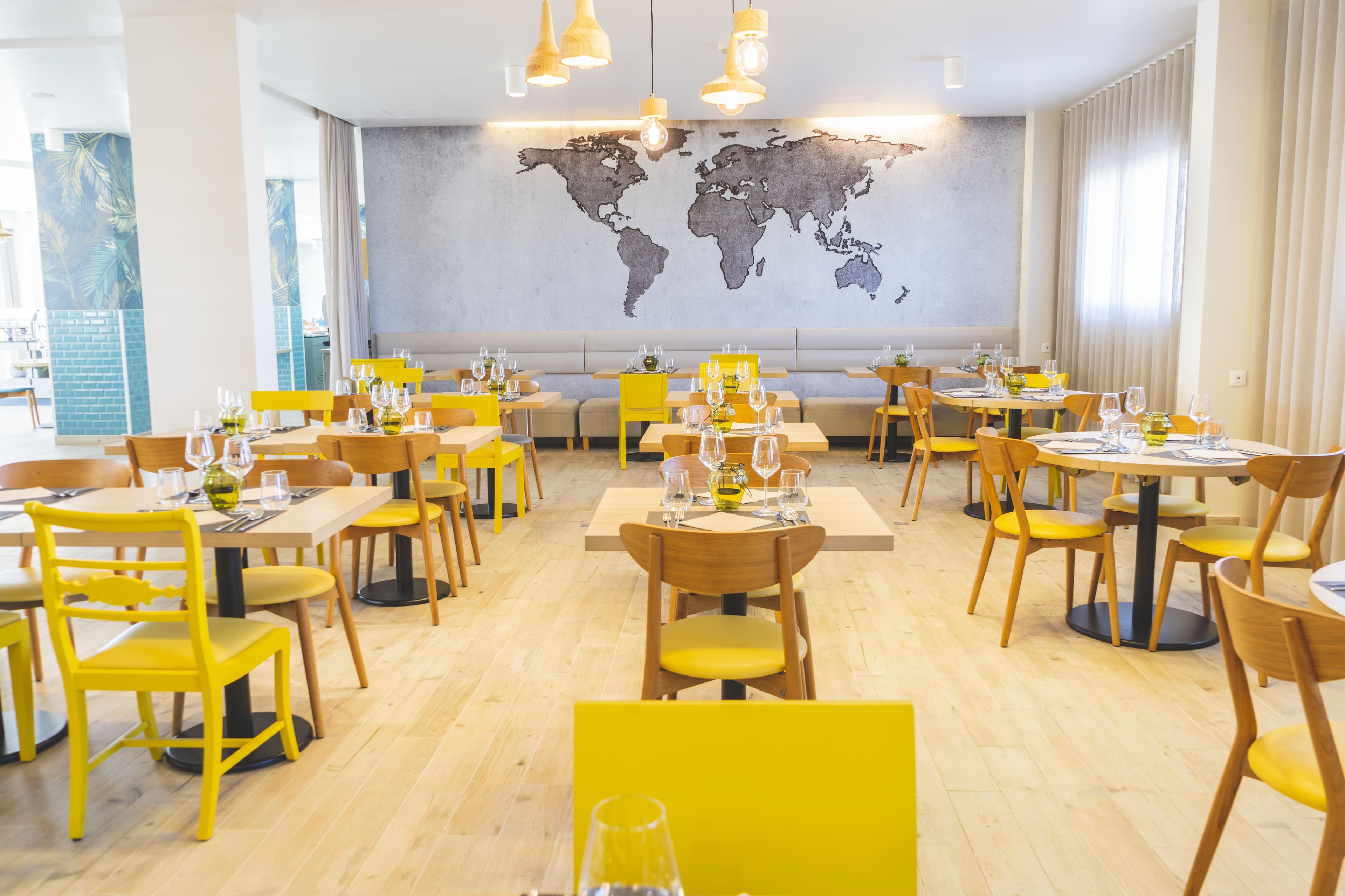 A restaurant with yellow chairs and tables, a world map on the wall, and hanging pendant lights.