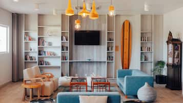 A modern living room with a flat-screen TV, bookshelves, a blue sofa, and a surfboard.
