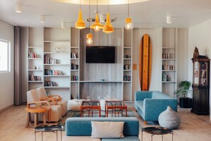 A modern living room with a flat-screen TV, bookshelves, a blue sofa, and a surfboard.