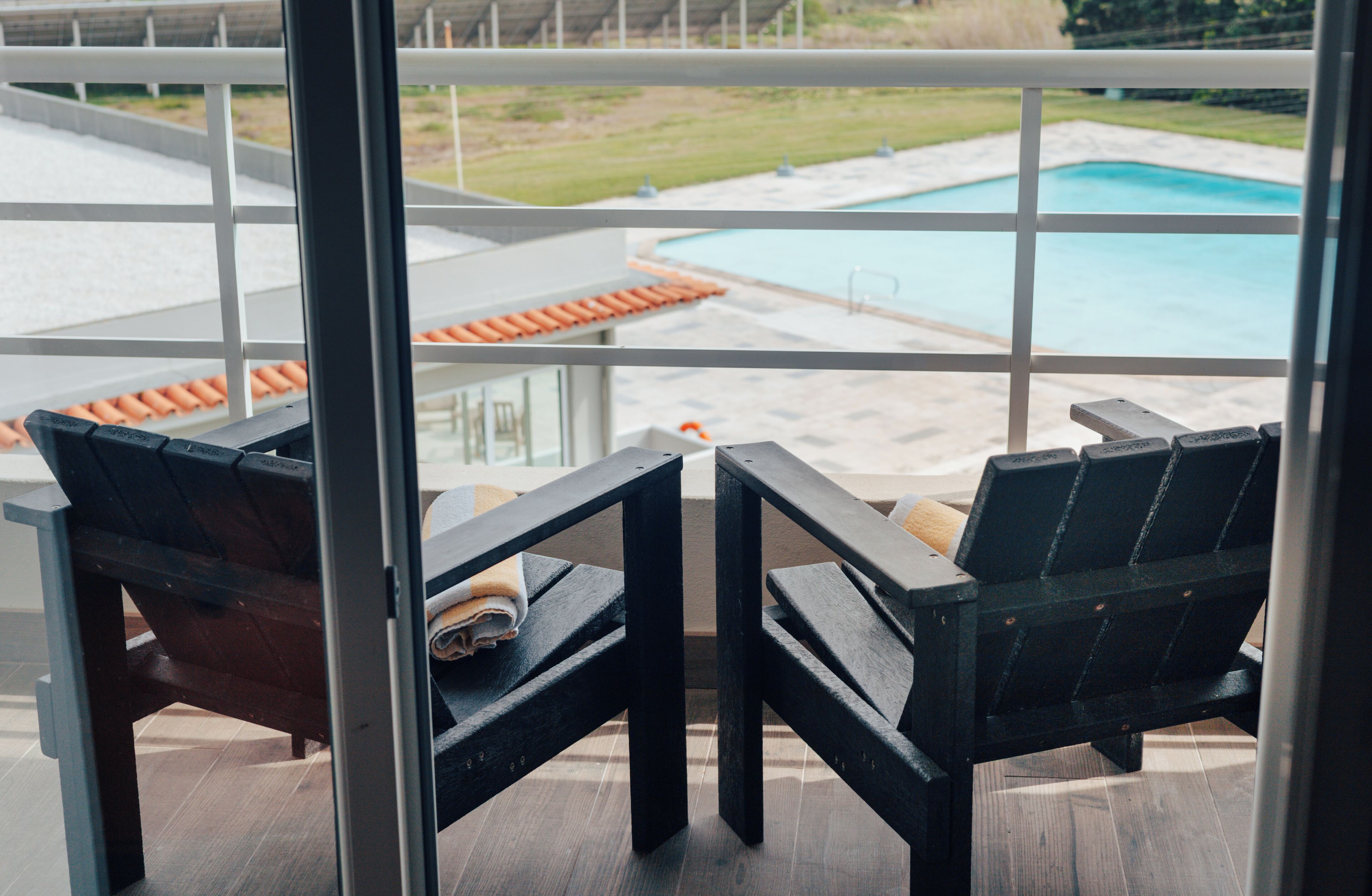 Un balcón con dos sillas de madera, vista a una piscina y zona ajardinada.