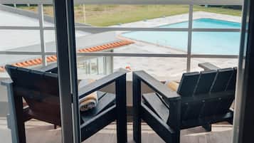 Un balcón con dos sillas de madera, vista a una piscina y zona ajardinada.