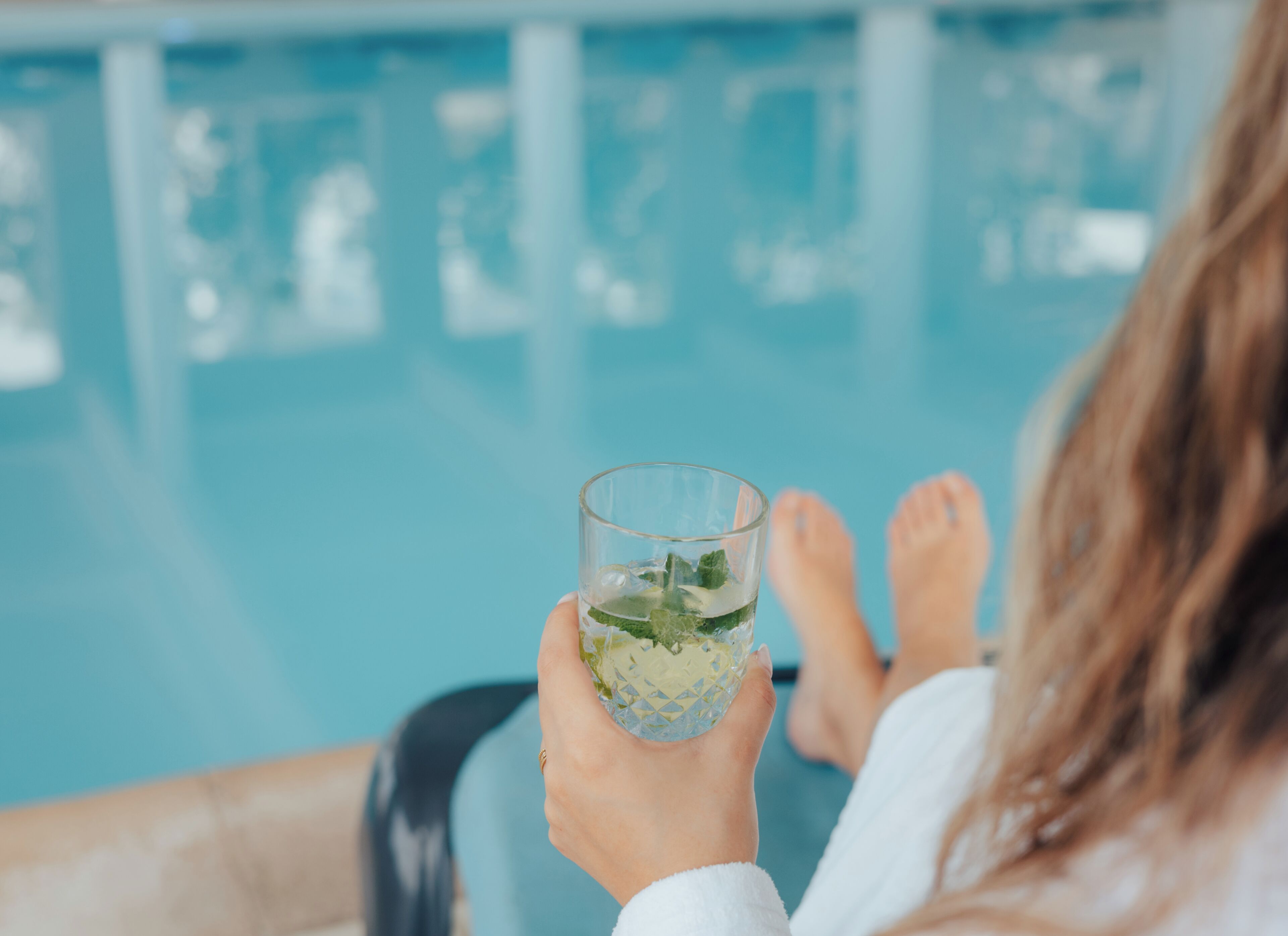 A person relaxing by a pool with a glass of water.