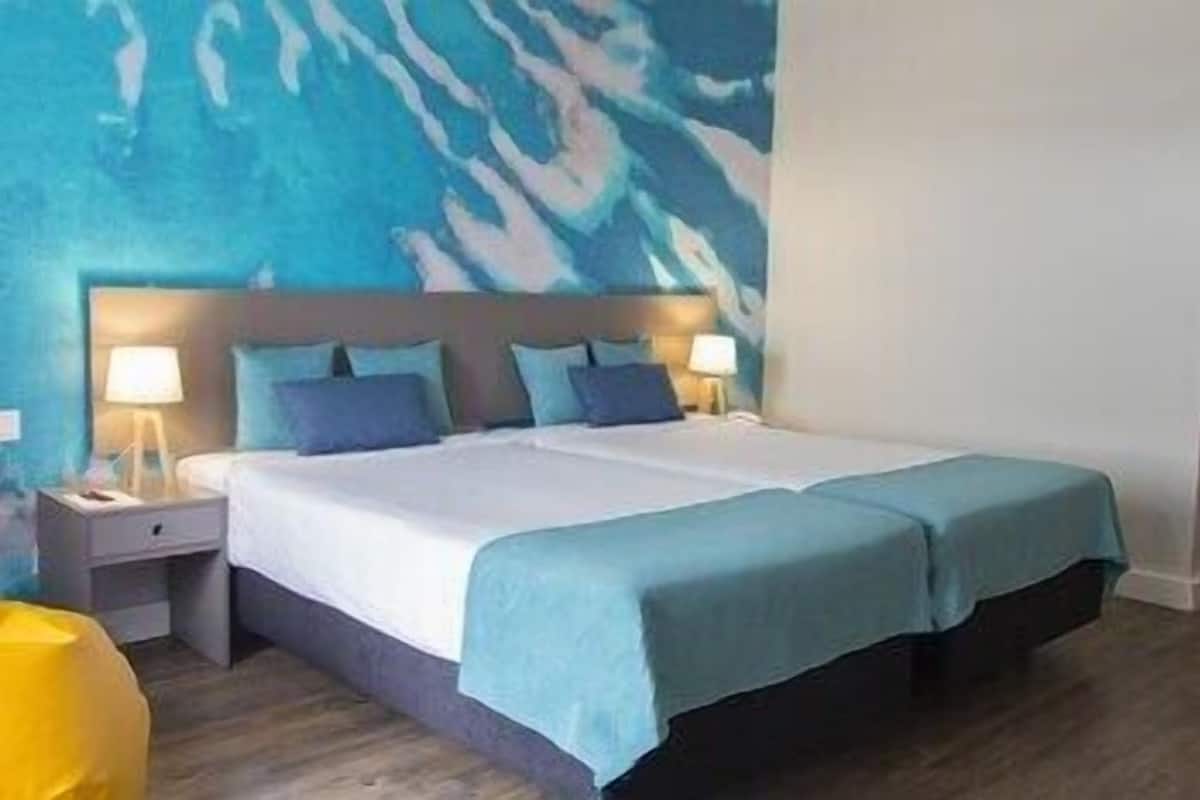 A double bed with a headboard, two bedside tables, and a wall with a blue abstract design.