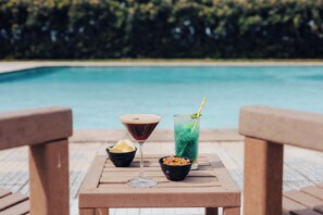 A table with a martini glass, a tall glass with a straw, and bowls of snacks by a poolside. - Star Inn Peniche (Peniche)