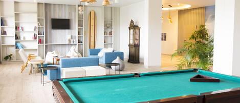 A pool table in a well-lit room with a sofa, bookshelves, and a television.