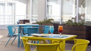 A bright outdoor seating area with yellow and blue chairs, a table with a drink, and a view of the sea through large windows. - Star Inn Peniche (Peniche)