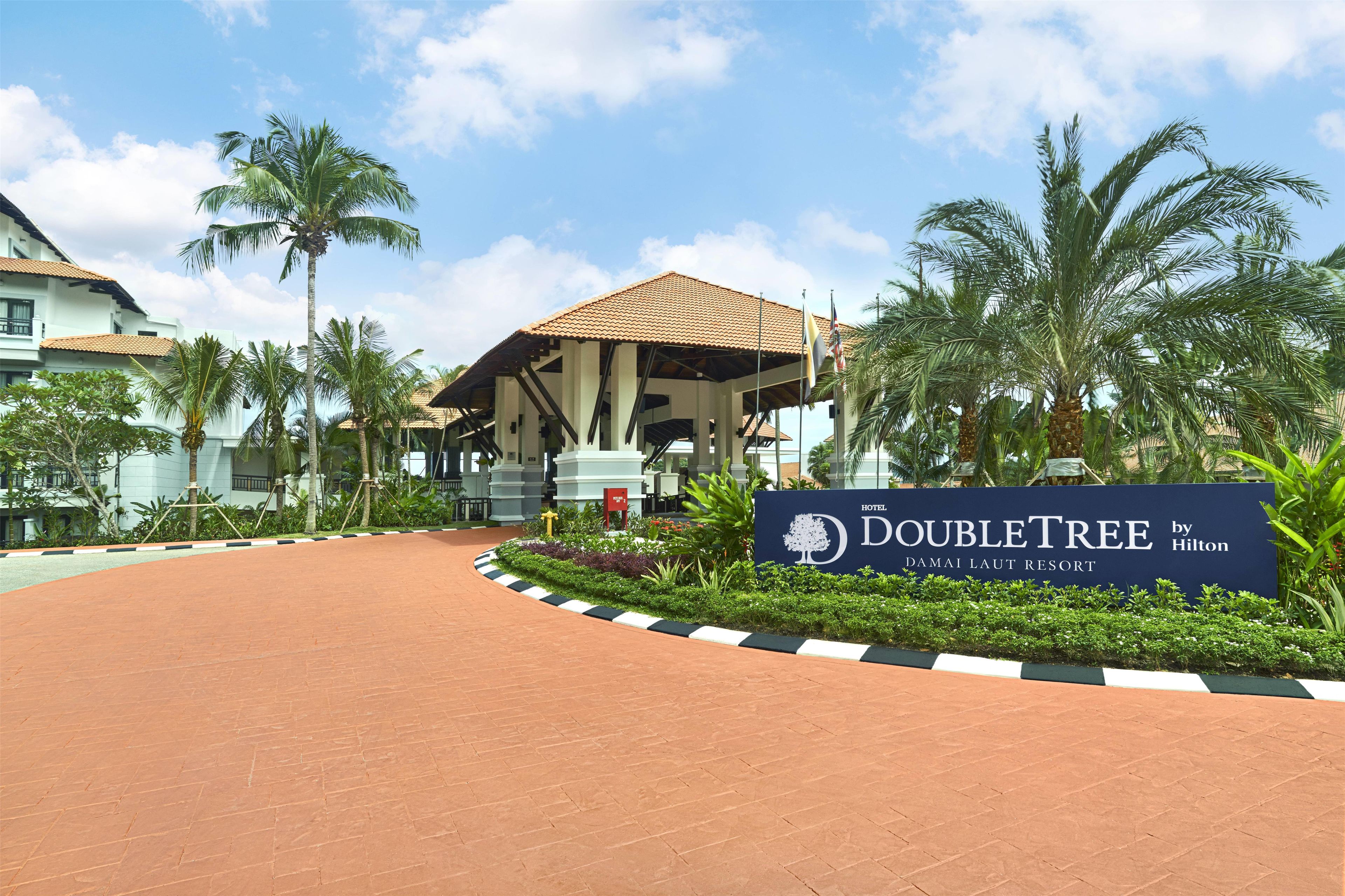 A hotel entrance with a sign for DoubleTree by Hilton, palm trees, and a building with a tiled roof.
