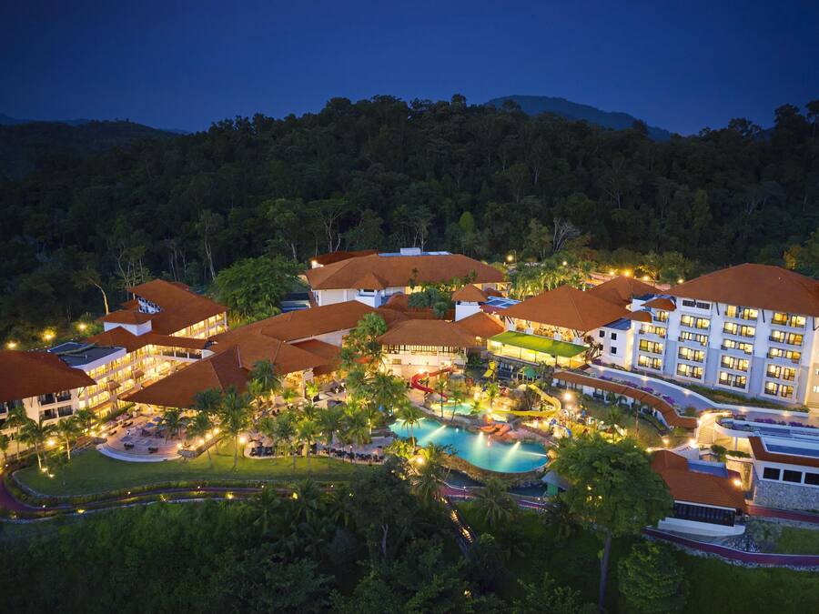A resort with multiple buildings, a swimming pool, and a mountainous backdrop.