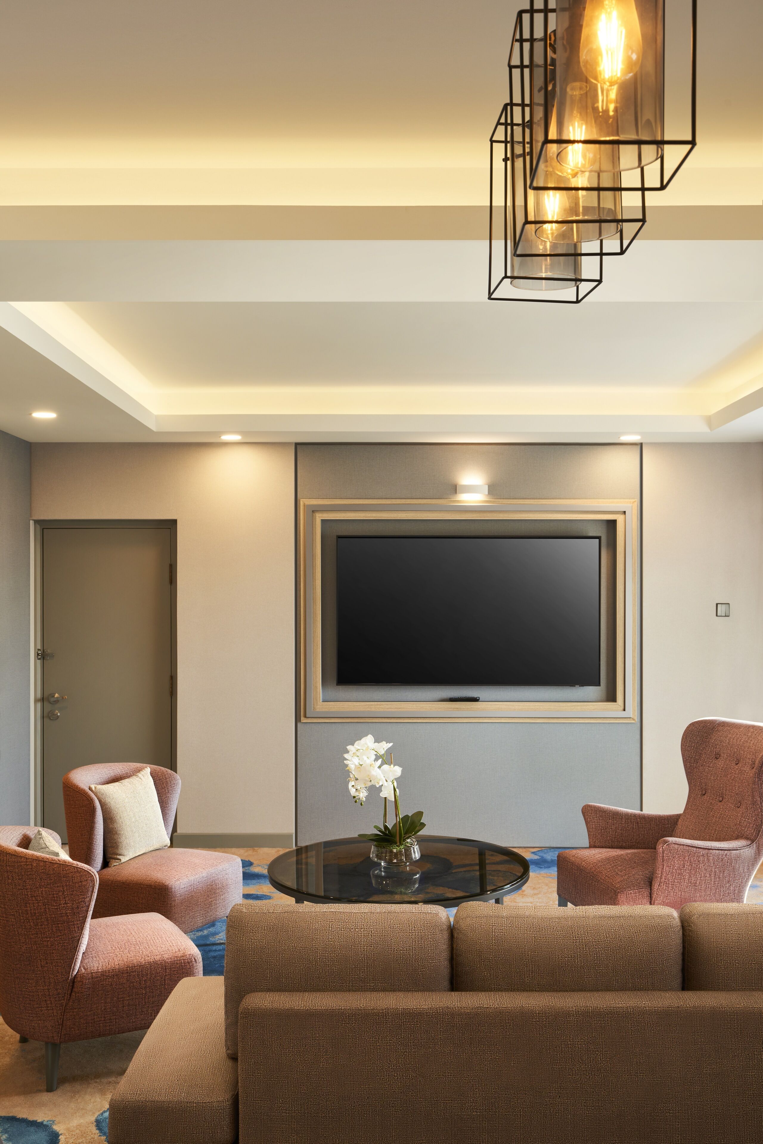 Un salon moderne doté d’un grand téléviseur à écran plat, de sièges confortables et d’un élégant luminaire suspendu.
